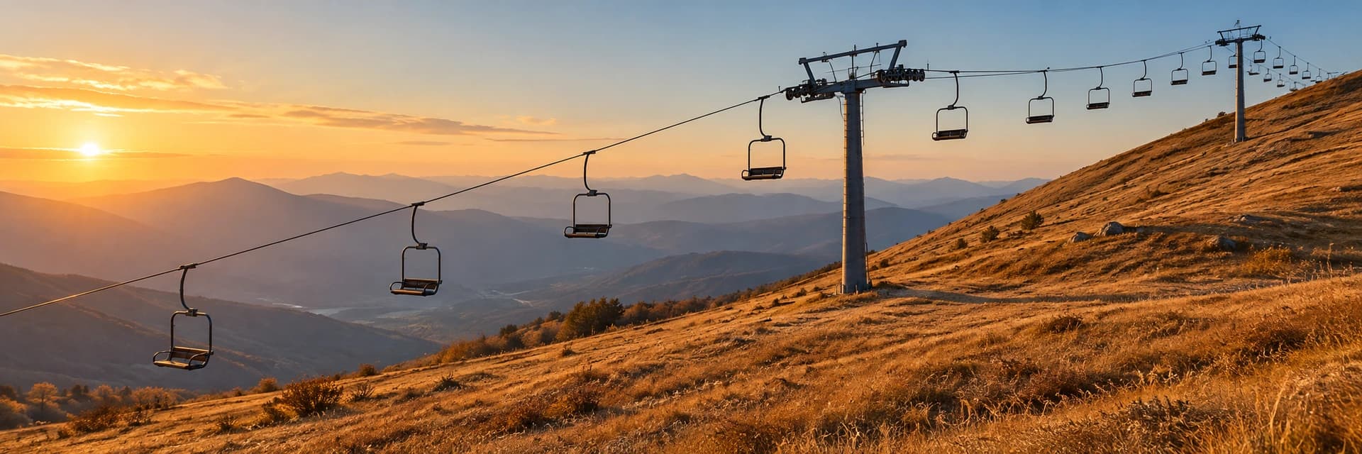 Editorial photograph at golden hour of an empty chairlift crossing a grassy autumn mountainside. A line of vacant chairs hangs from the cable past two lift towers, the low sun sits on the horizon at the left above a valley in soft blue haze, and the near tower casts a long shadow across the slope to the right. No people, no lettering, no logos and no buildings under construction appear anywhere in the frame.