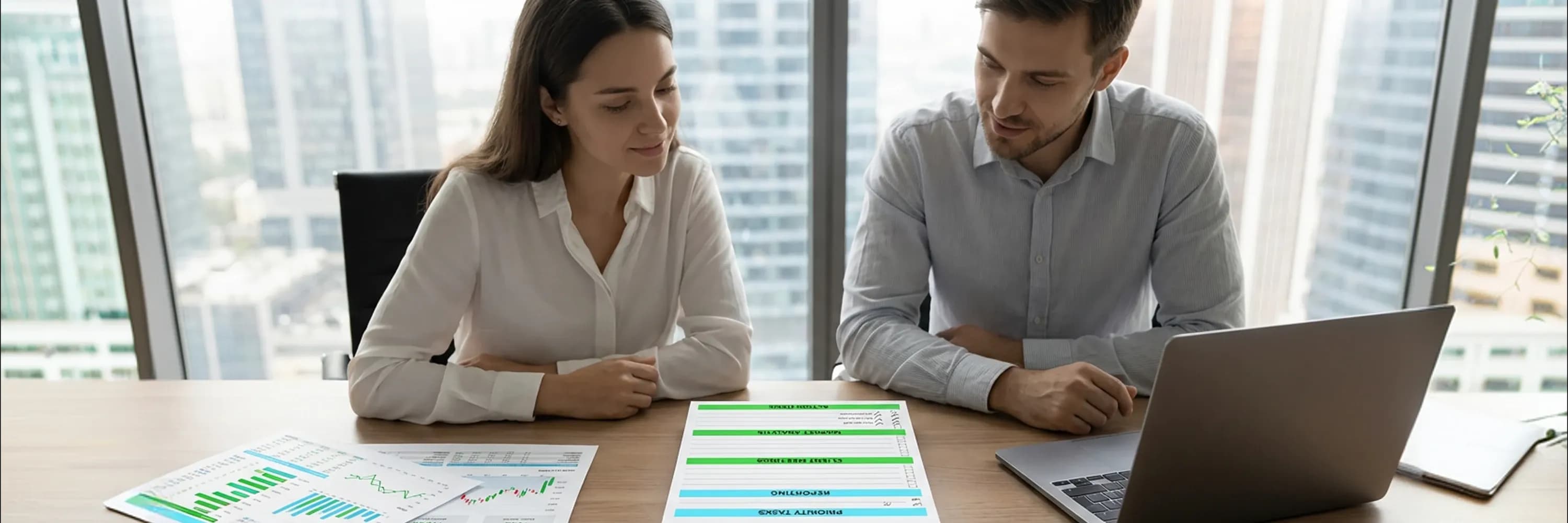 Two business professionals reviewing financial reports and performance charts during a strategy meeting in a modern office